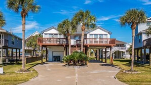 A beachfront property with a two-story house, a covered porch, and a small garden area.