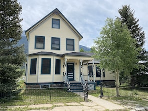 A two-story house with a porch, a small front yard, and a mountain in the background.