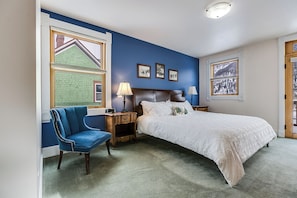 A bedroom with a large bed, a chair, a nightstand, and a window with a view of a building.