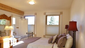 A bedroom with a bed, bedside lamps, a dresser, and a window with a view of trees. - Wildflower House - Silverton Victorian (Silverton)
