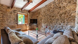 A cozy living room with stone walls, a wooden ceiling, a large sofa, a coffee table, and a TV. - QUIET RURAL HOUSE (San Juan)
