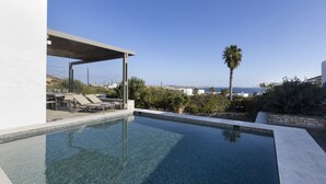 A rectangular swimming pool with clear water, surrounded by a white wall and a covered seating area with lounge chairs. - Villa Rinia - Seaview villa (Ampelas)