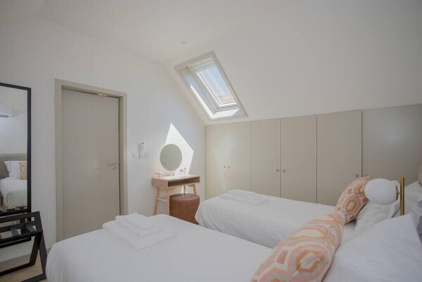 Une chambre avec deux lits, un puits de lumière, un miroir et une armoire.