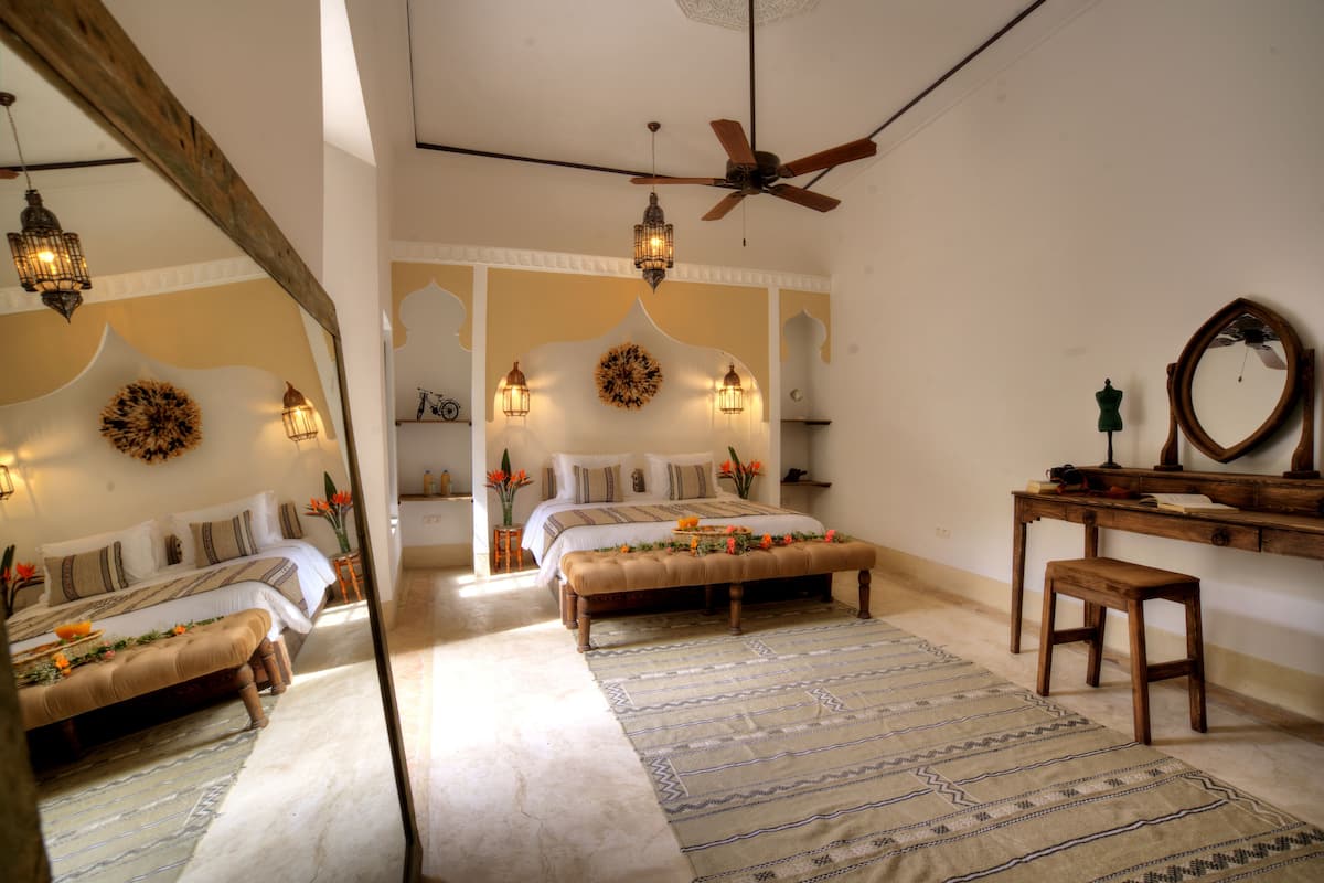 A bedroom with two beds, a ceiling fan, and a mirror on a wooden dresser.