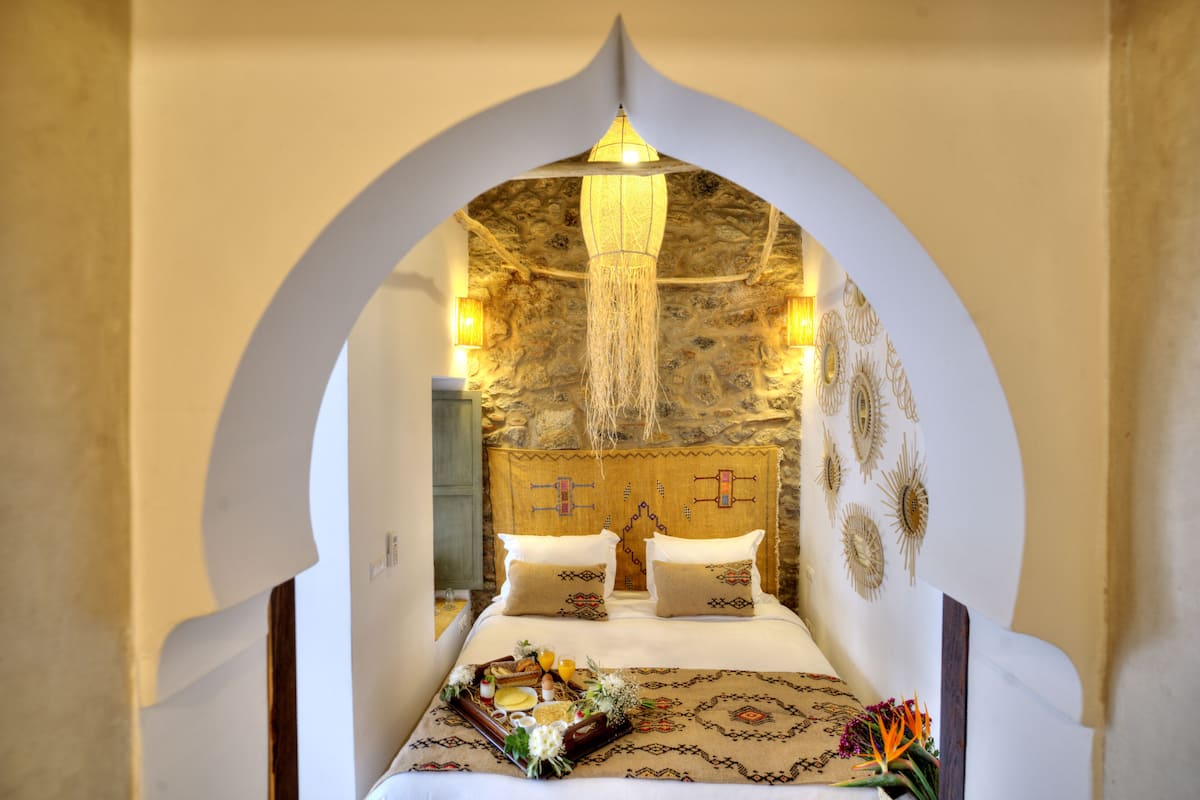 A bed with a decorative headboard, a tray with breakfast items, and a hanging light fixture.