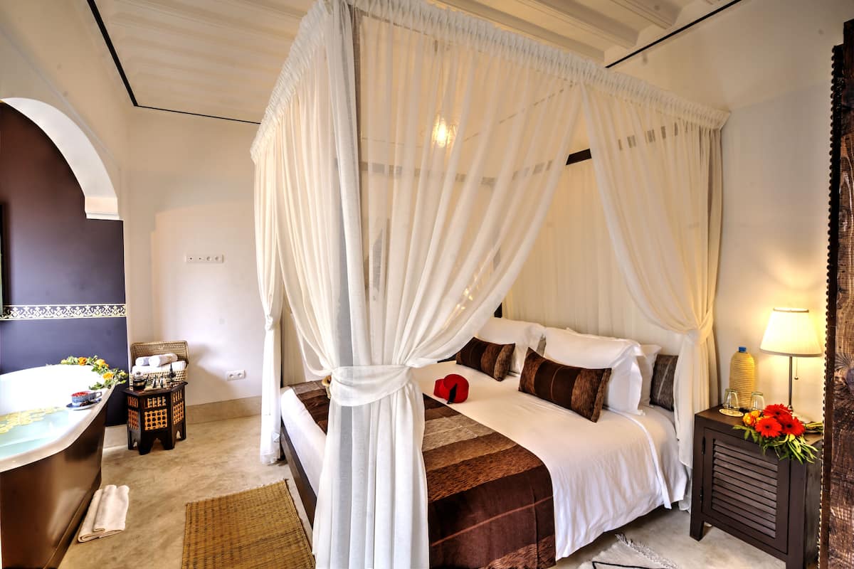 A bedroom with a four-poster bed, a bedside table with a lamp, and a small side table with flowers.
