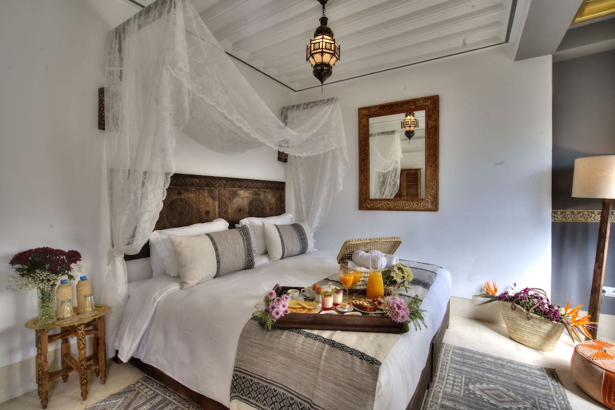 A neatly made bed with a tray of breakfast items, a bedside table with a vase of flowers, and a large mirror on the wall.