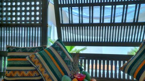 A room with a view through a window with a bamboo blind, a table with a fruit bowl, and patterned pillows. - Riad Sokera Hotel & Spa - Adults Only (Marrakech)