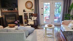 A modern living room with a fireplace, a sofa, a coffee table, and a view through a glass door to an outdoor patio. - Luxury home backyard paradise, salt water pool heated May to Oct. . 3bdrm 2 bath (Lindsay)