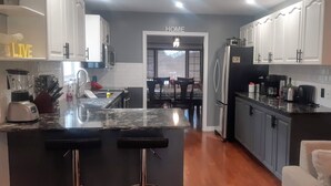 A modern kitchen with white cabinets, a black countertop, and a central island with bar stools. - Luxury home backyard paradise, salt water pool heated May to Oct. . 3bdrm 2 bath (Lindsay)