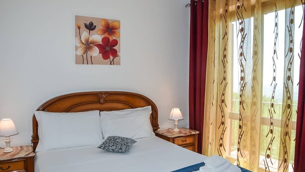 En snyggt bäddad säng med vita och blå sängkläder, två sänglampor, en dekorativ prydnadskudde och en tavla med blommor på väggen.