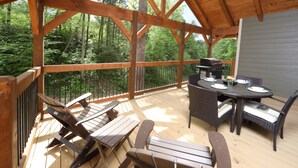 A wooden deck with a dining table and chairs, surrounded by a forest. - Head Over Hills (Gatlinburg)