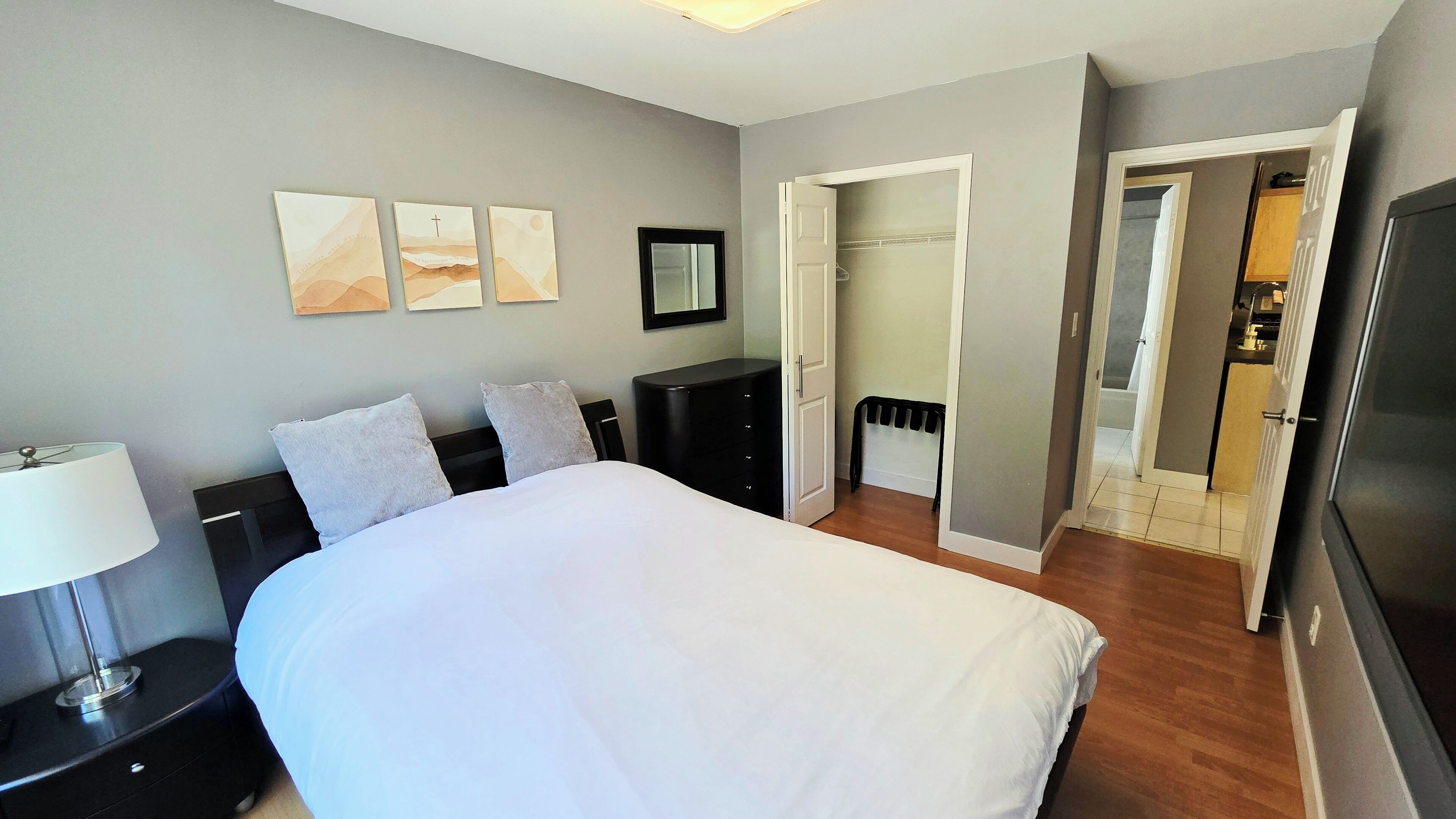 Une chambre à coucher avec un grand lit, une table de chevet, une commode et une armoire. Trois œuvres d’art sont accrochées au mur au-dessus du lit.
