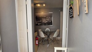 A hallway with a dining area featuring a table and chairs, a fire extinguisher, and a wall-mounted sign. - Modern, clean & private 1BR suite. Up to 4 guests. (Surrey)