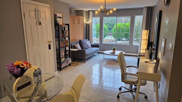 A living room with a sofa, a coffee table, a bookshelf, and a dining area with a table and chairs. - Modern, clean & private 1BR suite. Up to 4 guests. (Surrey)