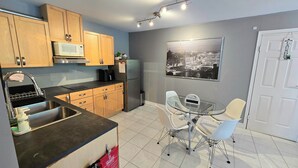 A modern kitchen with wooden cabinets, a stainless steel sink, a microwave, and a refrigerator. There is a glass table with chairs and a welcome sign. - Modern, clean & private 1BR suite. Up to 4 guests. (Surrey)