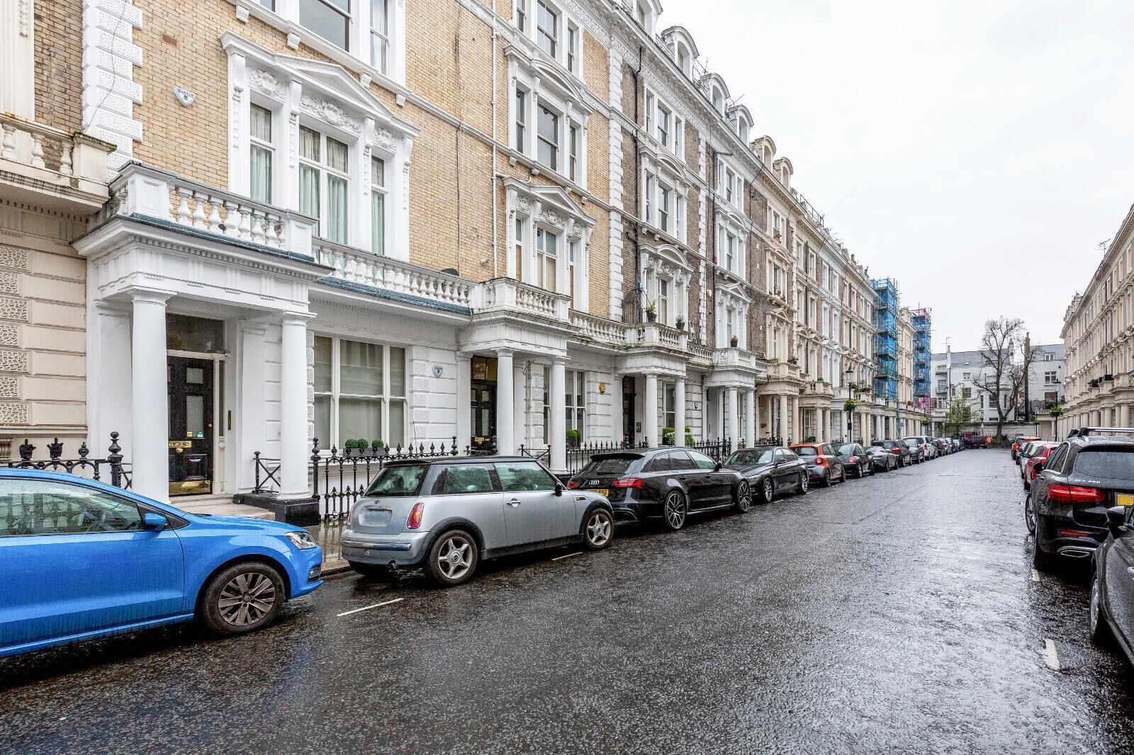 A row of traditional brick townhouses with white facades and multiple windows, parked cars on a wet street.