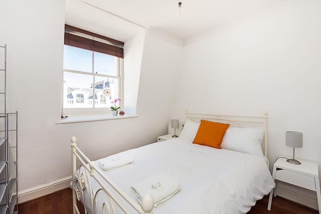 A white room with a bed, a window with a view, a bedside table, and a lamp.