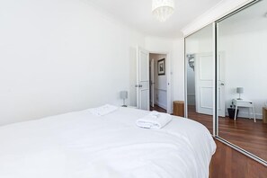 A hotel room with a large bed, a mirror, a small table with a lamp, and a door leading to another room. - Bright stylish Nott Hill apart sleeps 6 (London)