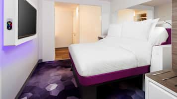A modern hotel room with a bed, a TV, and a desk.