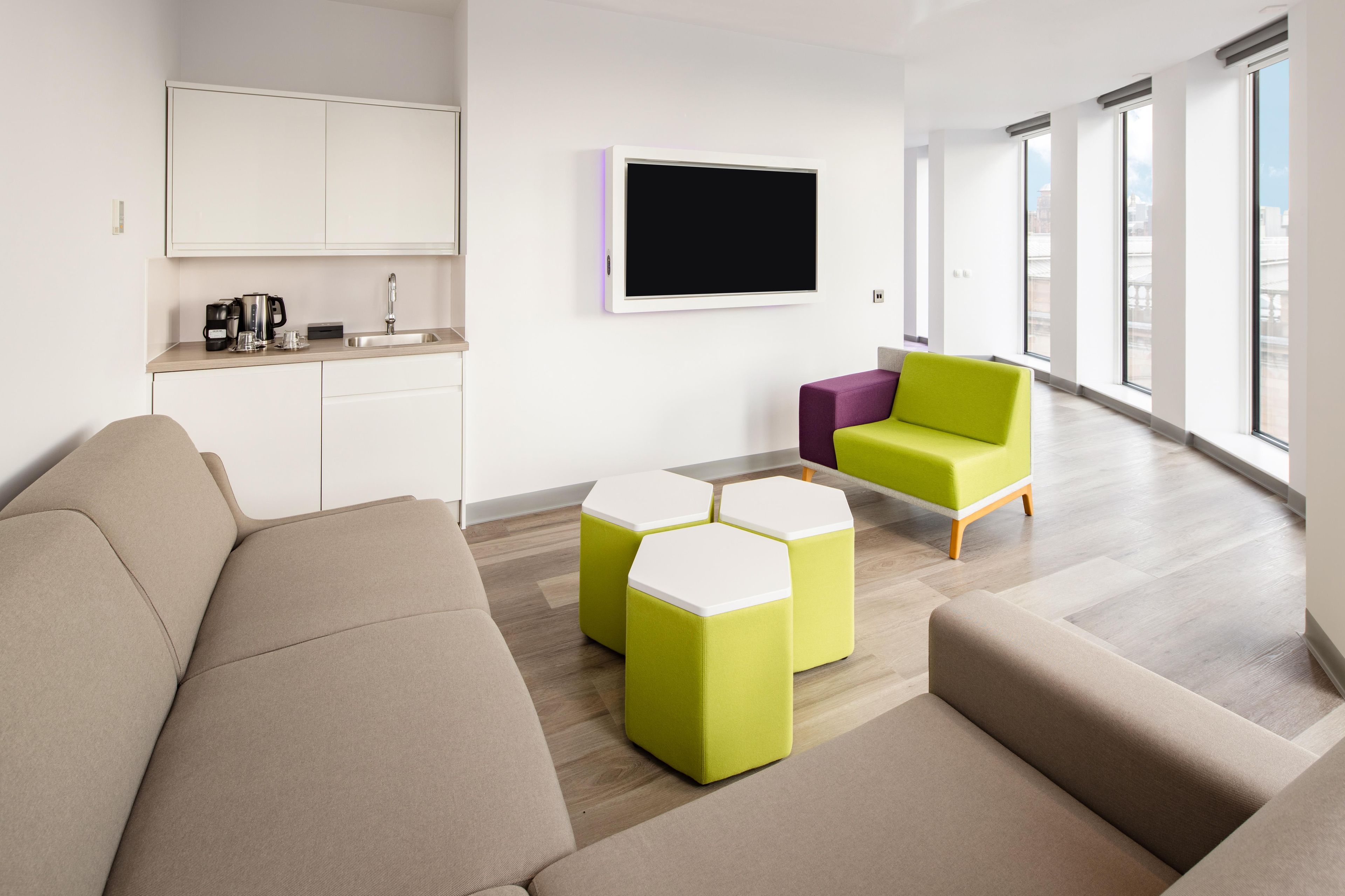 A modern living room with a sofa, ottomans, and a coffee station.