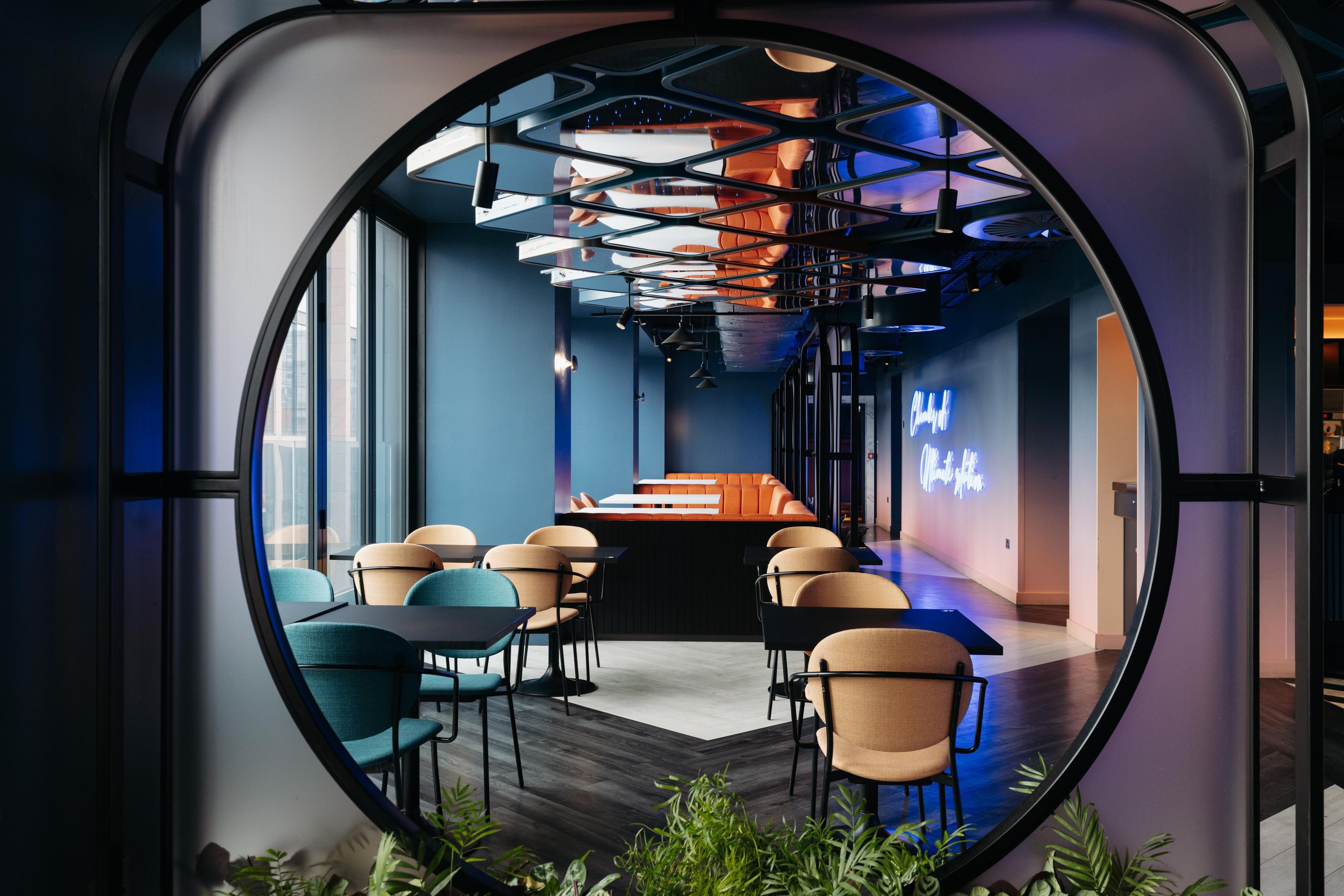 Un intérieur moderne doté d’un espace circulaire offrant une vue panoramique, de sièges, de tables et d’un panneau lumineux au néon.