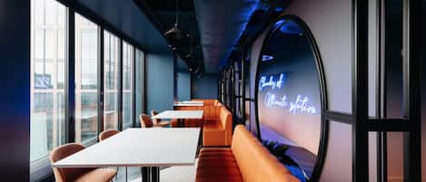 Een modern interieur met een lange tafel, oranje zitplaatsen, grote ramen en een neonbord.