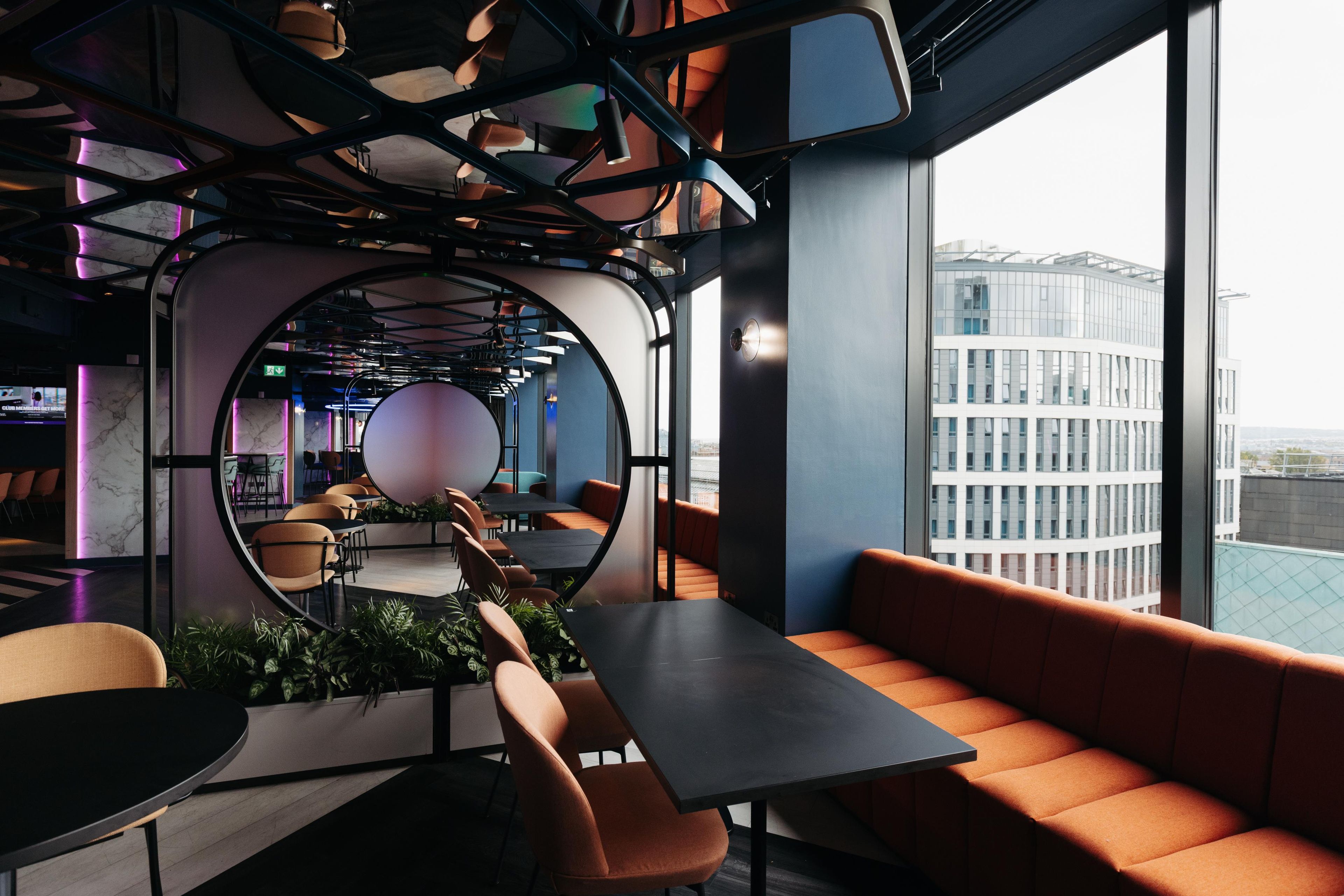 A modern interior with a circular seating area, tables, and a view of a cityscape through large windows.