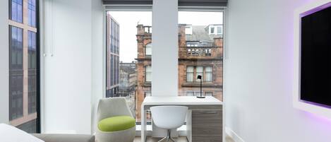 Ein modernes Schlafzimmer mit Bett, Schreibtisch und Stuhl, mit großen Fenstern und Blick auf die Stadt.