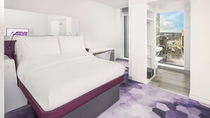 A modern hotel room with a large bed, a bedside table, a mirror, and a view of the city through a large window. - YOTEL Glasgow (Glasgow)