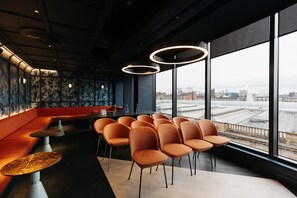 A modern interior with a seating area, a bar, and large windows offering a city view.