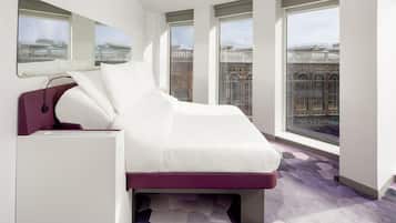 Habitación de hotel moderna con cama, escritorio y ventanas amplias que ofrecen vistas de la ciudad.