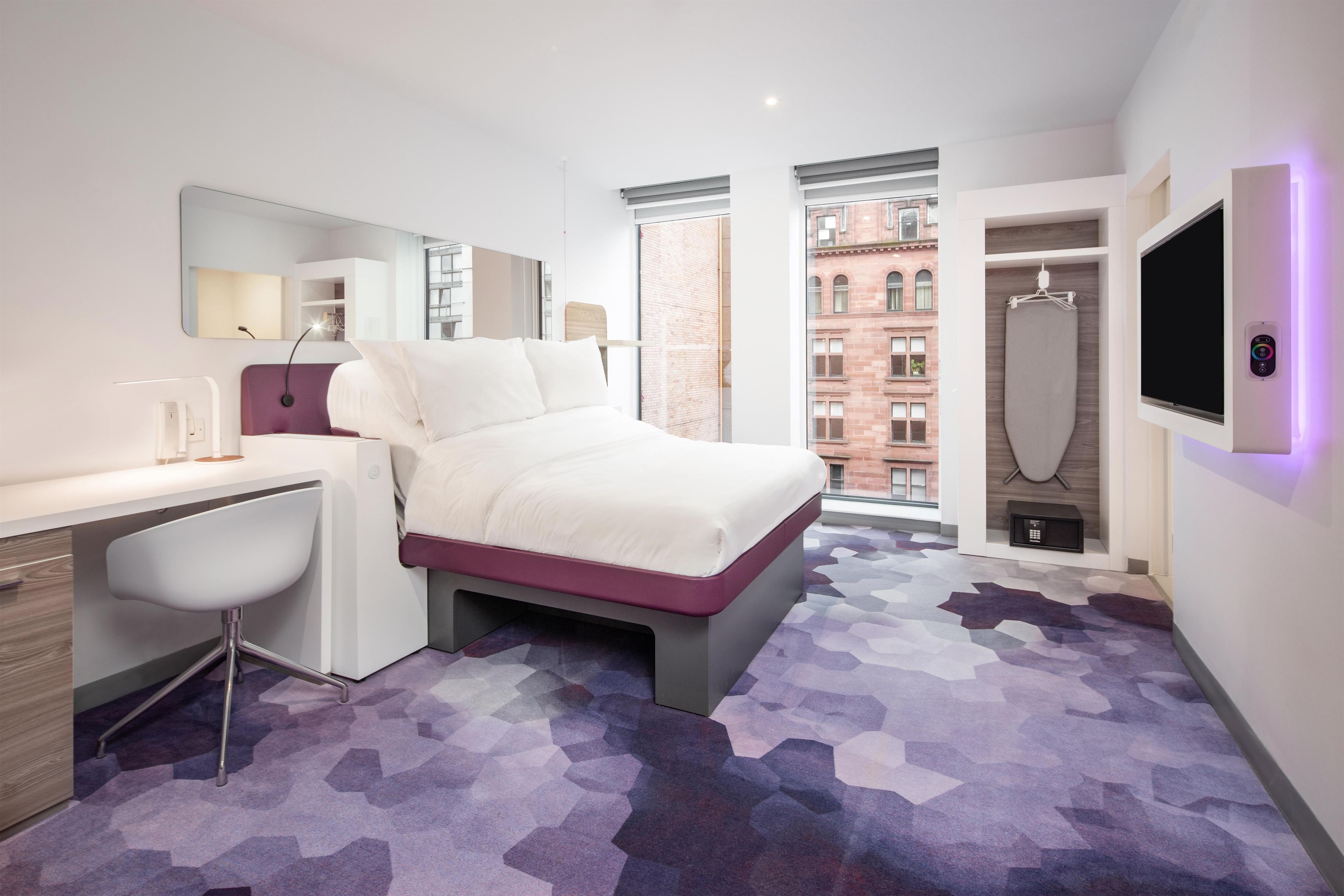 Une chambre d’hôtel moderne équipée d’un lit, d’un bureau, d’une chaise, d’une grande fenêtre et d’un téléviseur.