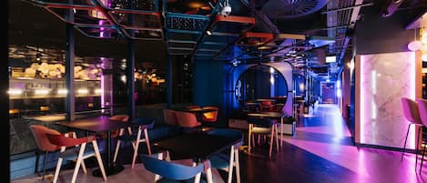 Un interior moderno con diversas opciones de asientos, incluidas mesas y sillas, y una zona de bar visible a través de un separador de vidrio.