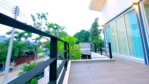 Un edificio moderno con balcón, ventanas amplias y vistas a zonas verdes y otros edificios.