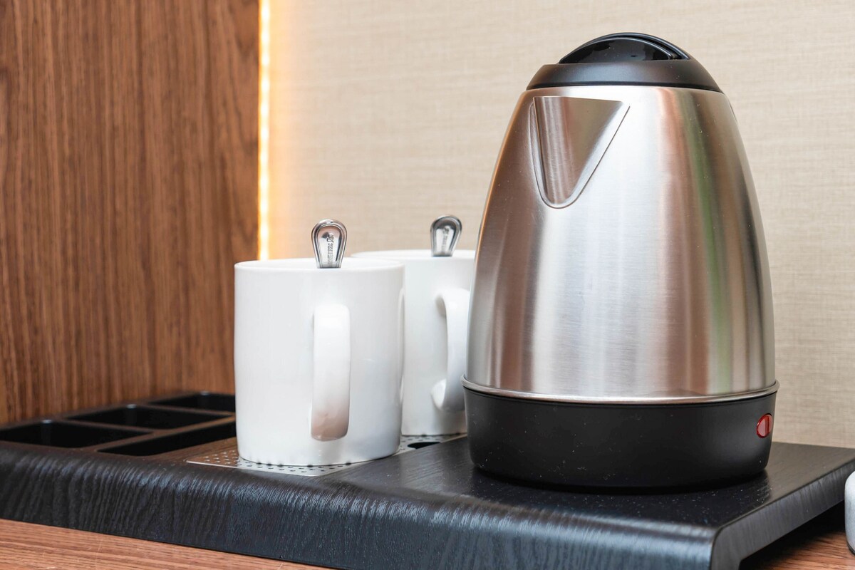A stainless steel kettle on a black tray with two white mugs beside it.