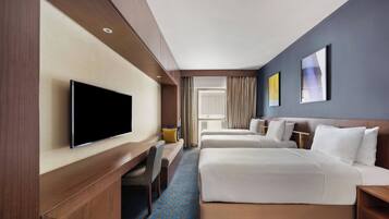 Habitación de hotel con dos camas, televisión, escritorio y ventana con cortinas.