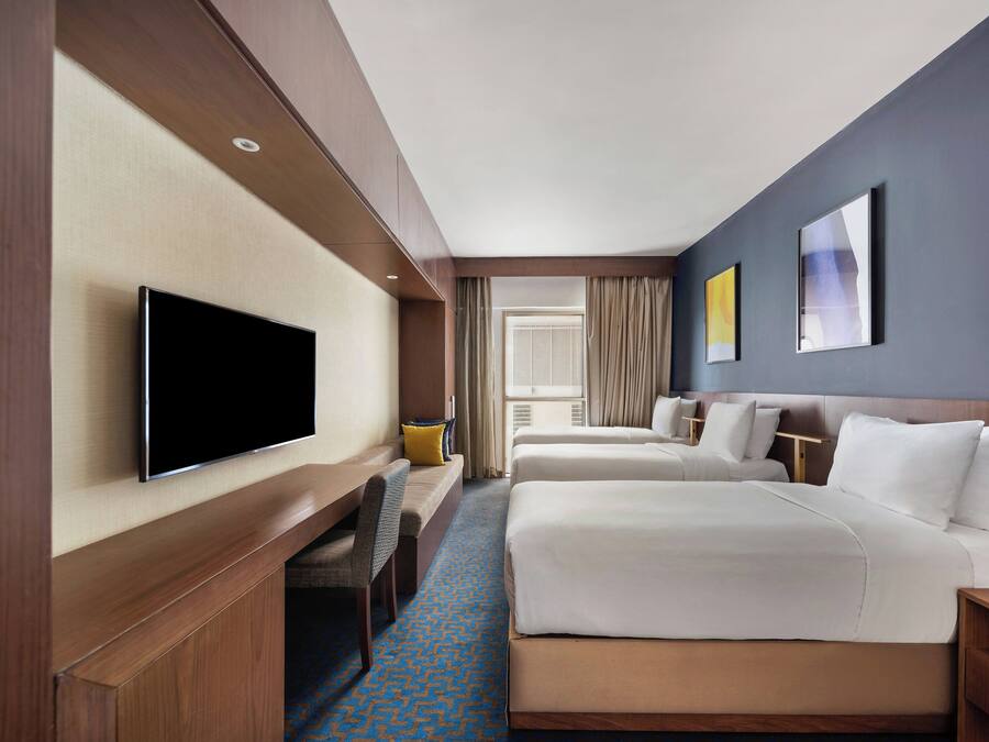 Habitación de hotel con dos camas, televisión, escritorio y ventana con cortinas.