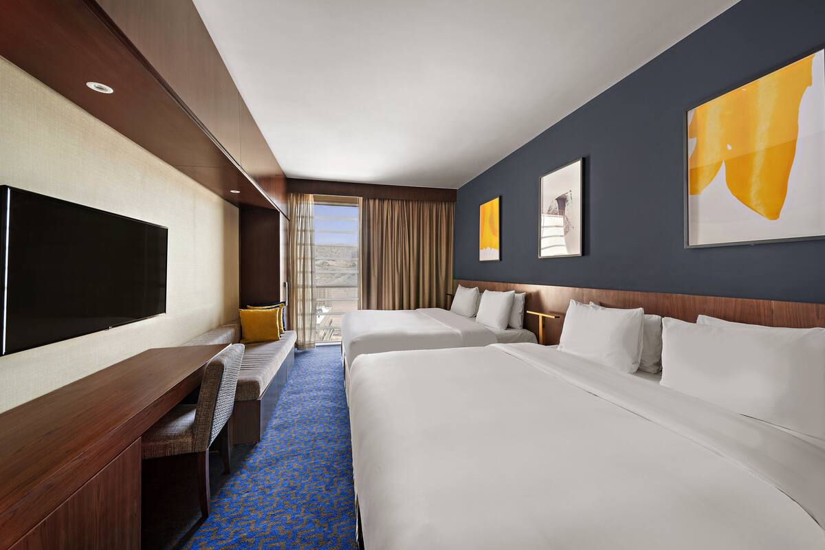 Une chambre d’hôtel avec deux lits, un téléviseur à écran plat, un banc et une vue sur l’extérieur.