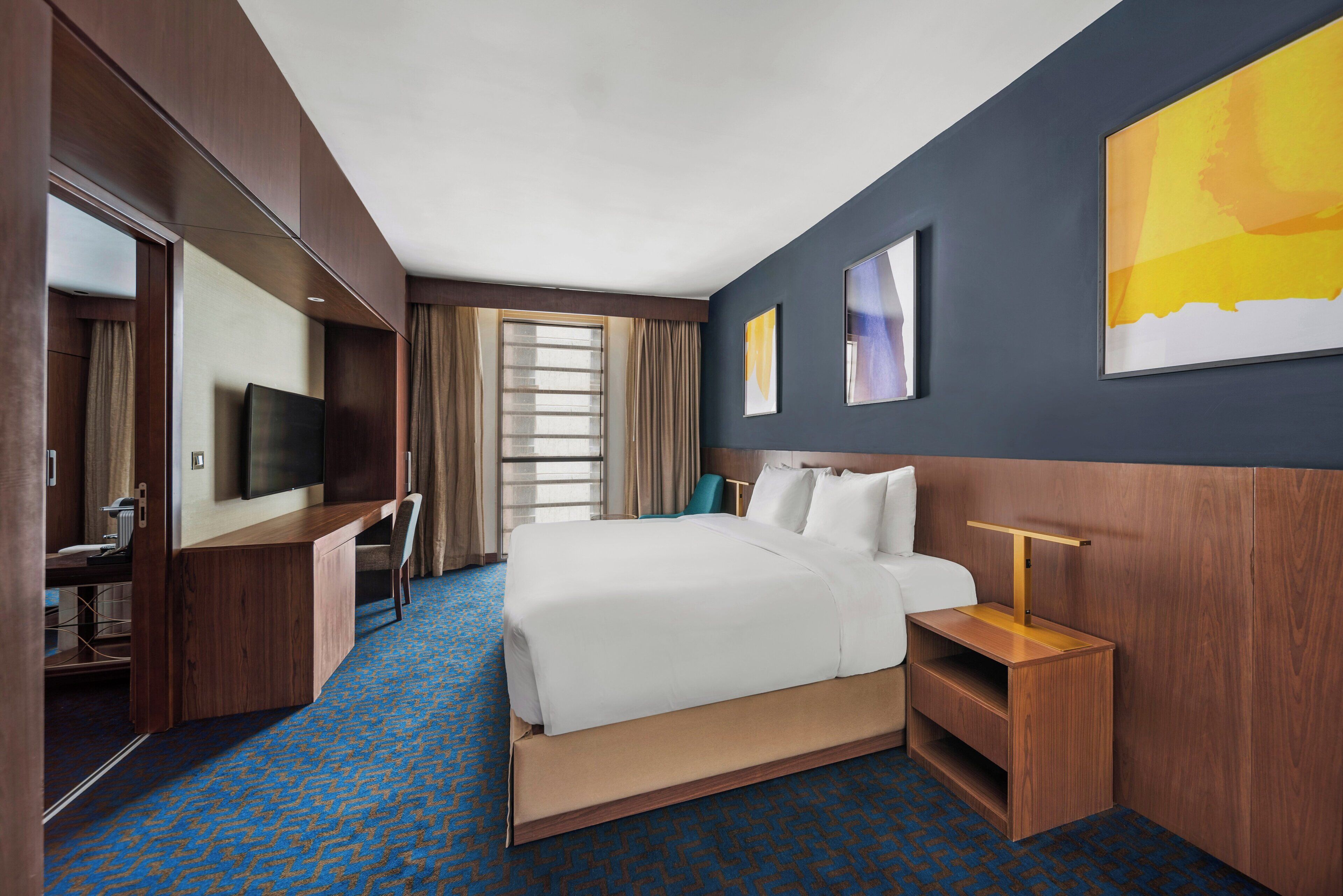 A hotel room with a bed, a desk, a TV, and a window with curtains.