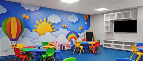 Un salón infantil con muebles coloridos y un mural de nubes, sol y globos aerostáticos.