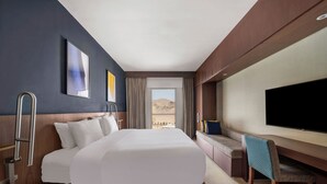 Habitación de hotel con una cama grande, un escritorio, una silla, un televisor de pantalla plana y vistas al desierto.
