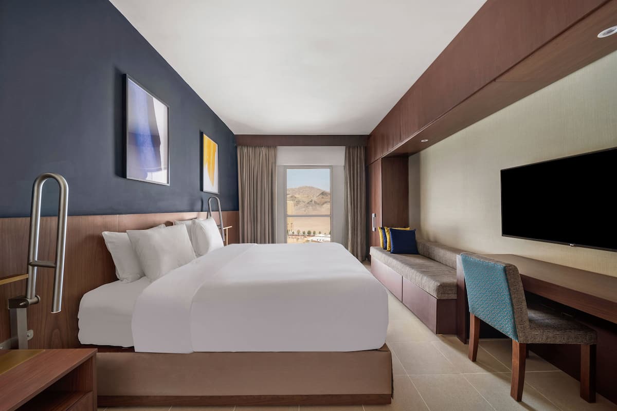 Une chambre d’hôtel avec un grand lit, un bureau, une chaise, un téléviseur à écran plat et une vue sur le désert.