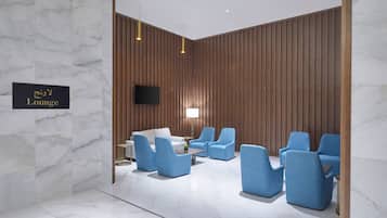 Un área de descanso con pared de mármol, paneles de madera y asientos azules.