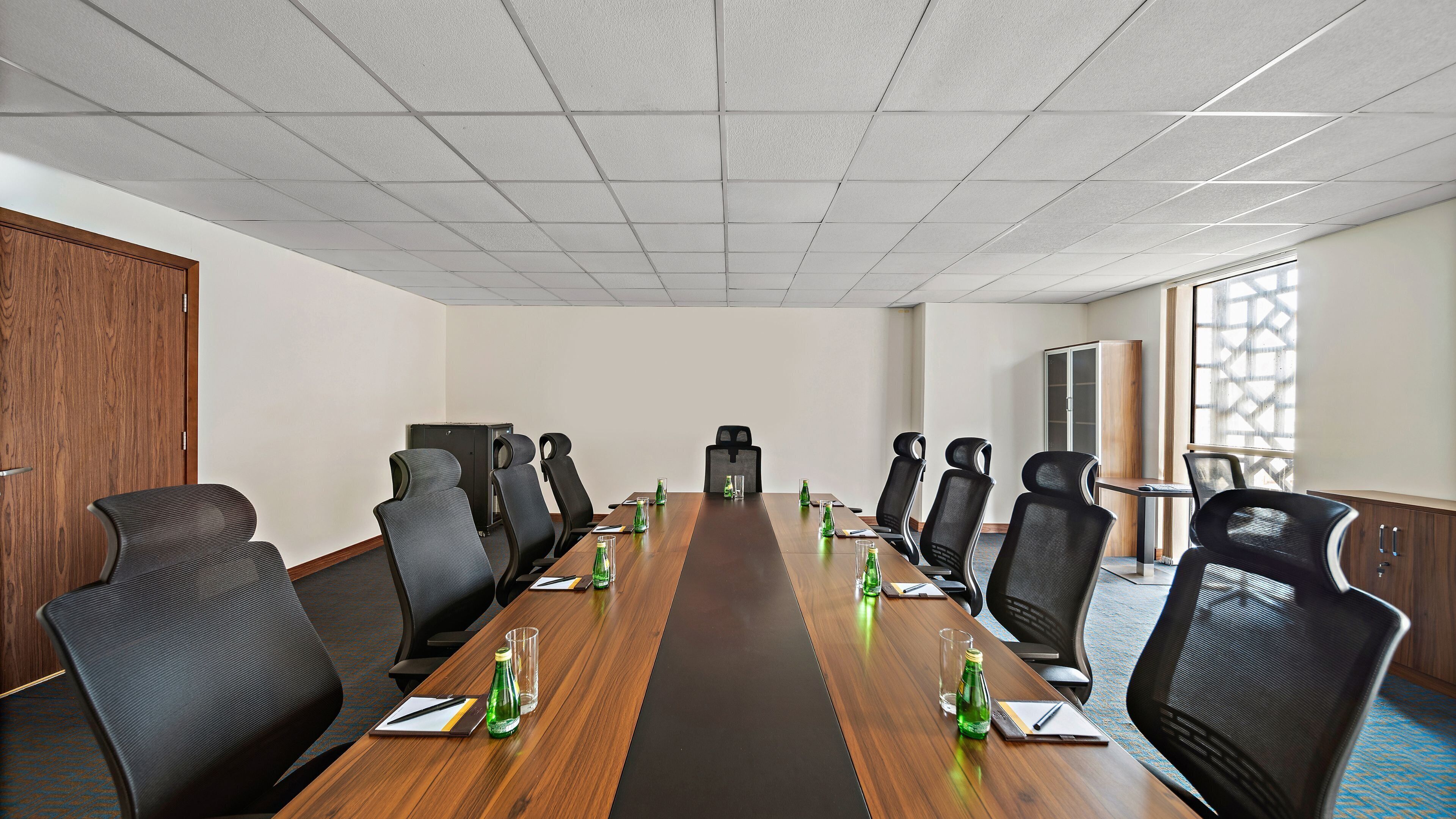 A conference room with a long table, multiple chairs, and a projector screen.