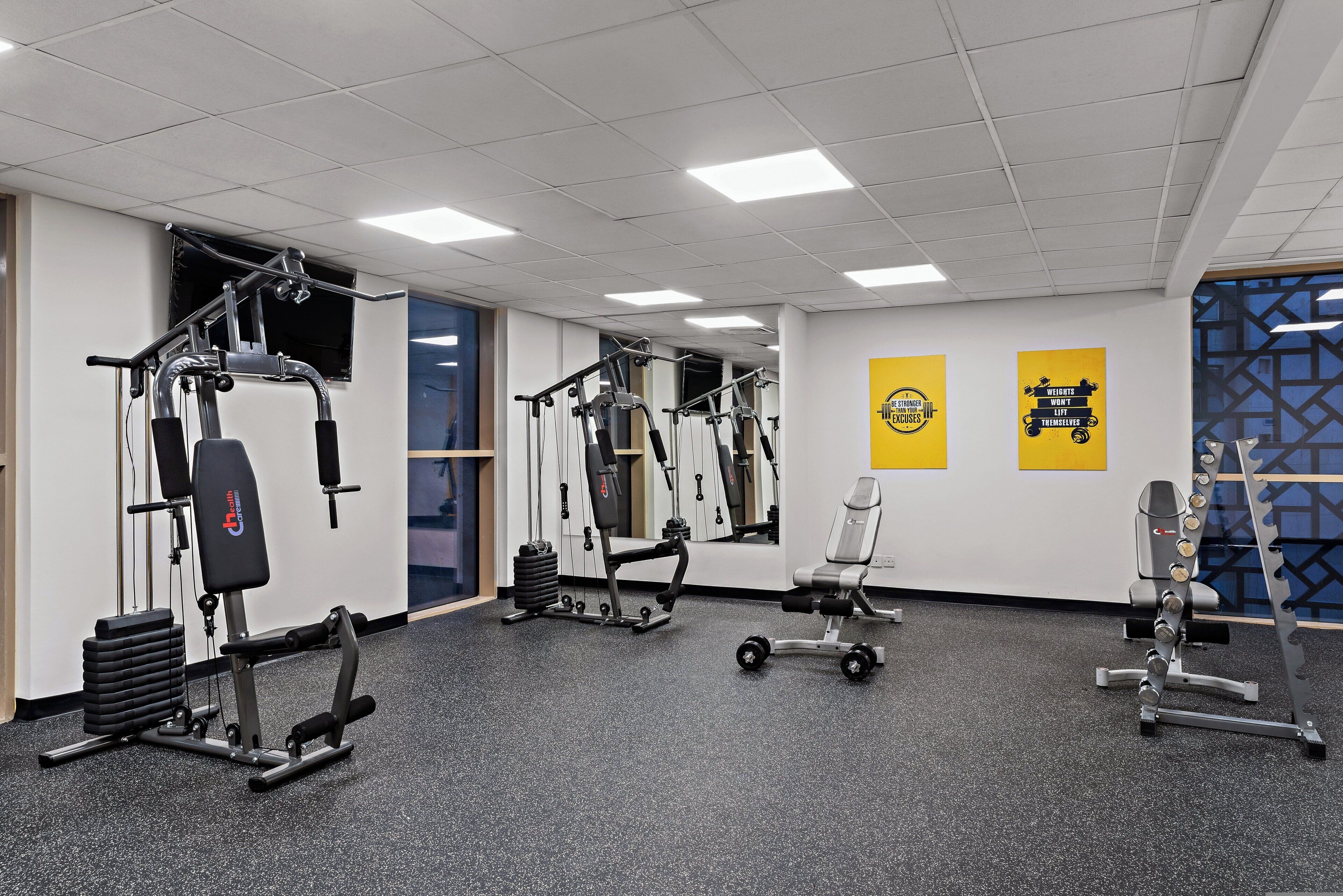 Une salle de sport équipée de divers appareils d’exercice, d’un miroir et de posters motivants accrochés au mur.