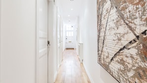 Un couloir aux murs blancs, doté d’un plancher en bois et orné d’un grand tableau abstrait sur le mur de droite.