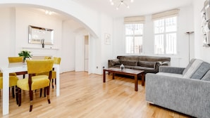 Un salon spacieux doté d’un parquet, d’un canapé gris, d’un canapé marron et d’un coin repas avec des chaises jaunes et une table blanche.