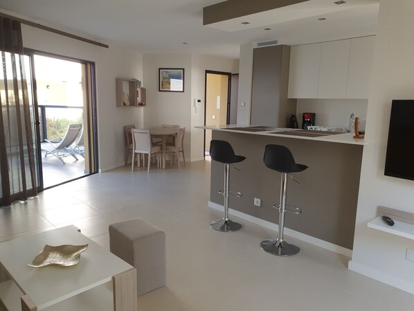 A modern kitchen with a dining area, bar stools, and a large window.