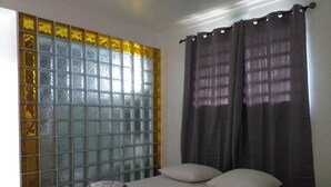 Una camera da letto con un letto, due cuscini, un comodino, una finestra con pannello decorativo e una tenda.
